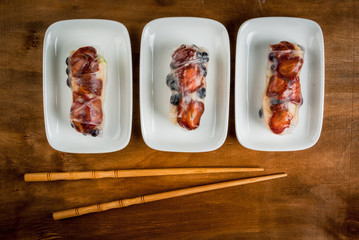 Sweet spring rolls with fruits and berries on the classic wooden table, next to chopsticks for sushi, close view, copy space