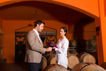 Winemaker with expert woman oenologist chemist in winery cellar.