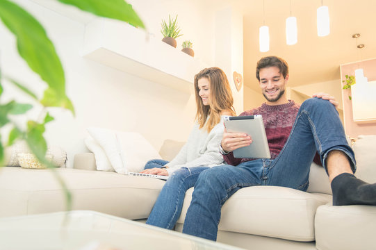 Happy couple using pc and tablet sitting on the sofa at home - Powered by Adobe