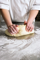 Woman knead the dough in bakery, on a table from steel. Working process