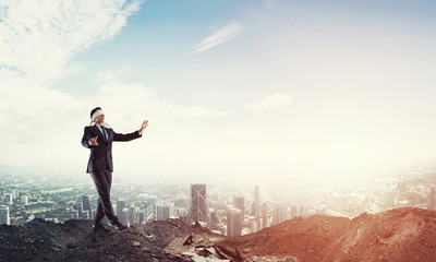 Young businessman in blindfold walking carefully and cityscape at background