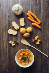 Vegetable soup in white bowl surrounded by ingredients on wooden table