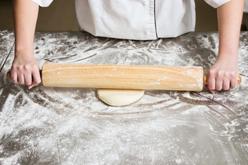 Woman unrolls dough in bakery, on a table from steel. Working process.