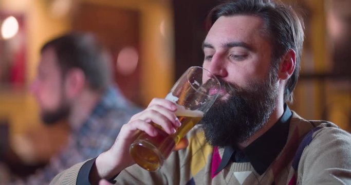 Bearded man drinks beer at pub bar counter 4k close-up video. Male guest taste and enjoy lager.  Alcohol beverage concept