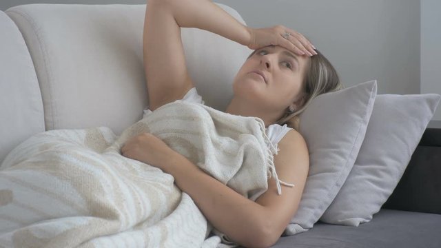 Young woman suffering from headache lying on sofa and touching forehead. Footage shot at 4K resolution