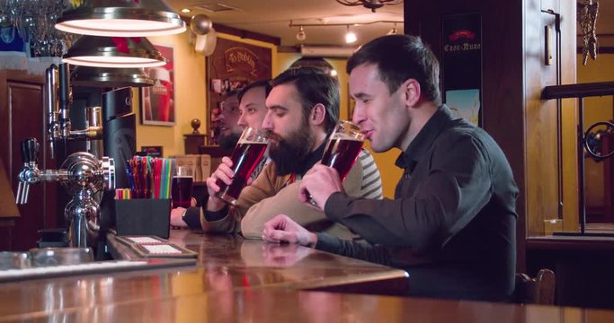 Friends group talks and drinks beer at pub bar 4k close-up video. Men having fun, drinks brown lager or ale from glasses