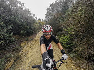 POV, Original point of view. Happy Young man on bicycle take a selfie with action cam and selfie stick. Training on mountain bike on a mountainous road in a rainy day