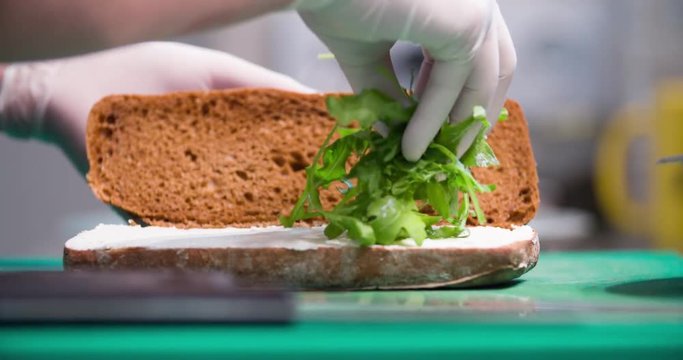 Sandwich cooking 4k video: chef puts herbs arugula rucola between slices of brown bread.  Food preparing in restaurant