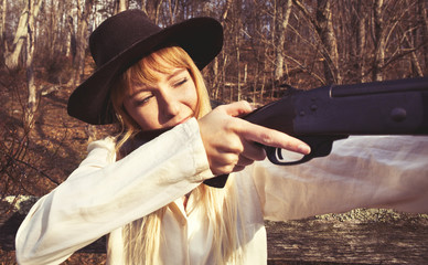 Young blond woman holding up a gun in the woods