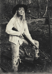 Young blond woman holding a gun standing in the woods