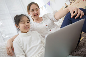 Asian mother and daughter using laptop together in bedroom