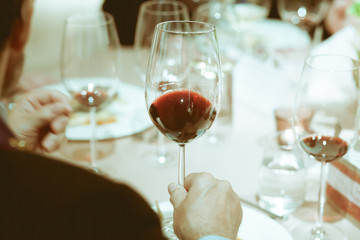 blurry background, red wine in hand of man on the table on dinne