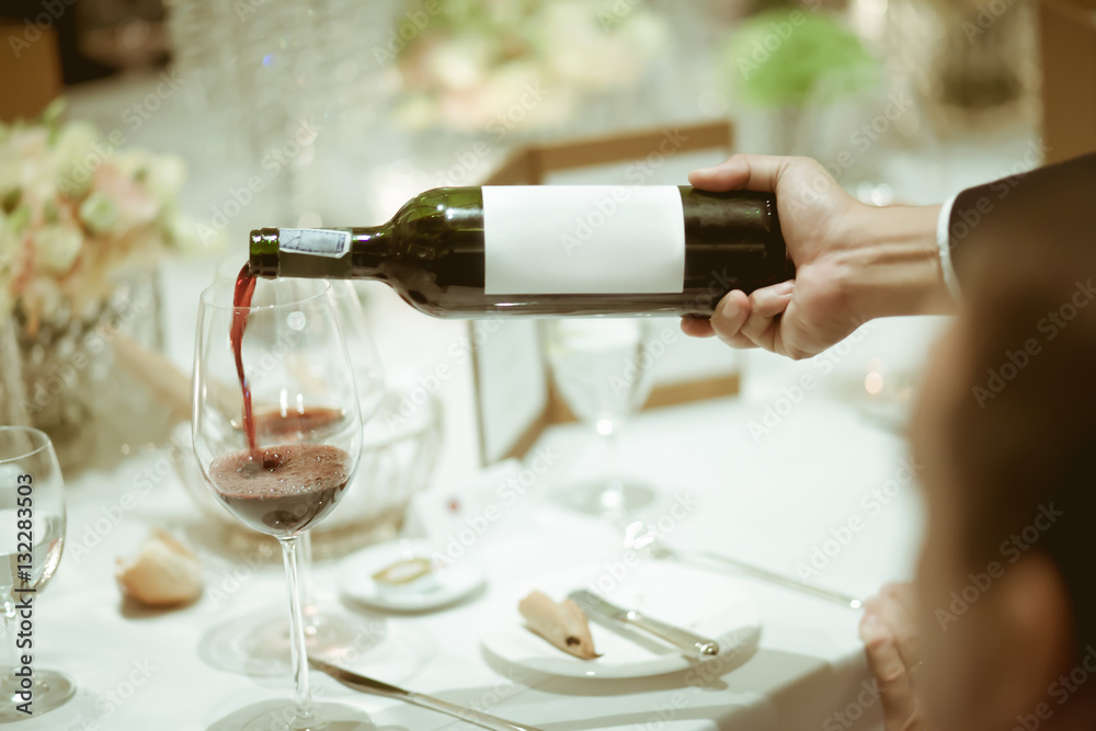 Wall mural waiter pouring red wine in wine glass on the table for service i