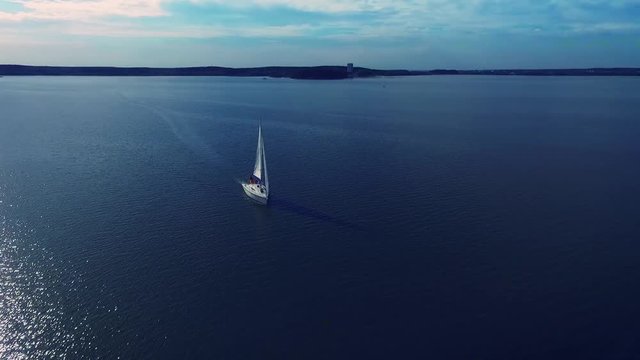 Lonely white yacht, which is floating in the rays of the sun. Shooting with the drone. Blue water.