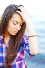 Portrait of pensive beautiful woman in a plaid shirt with drooping eyes by the sea.
