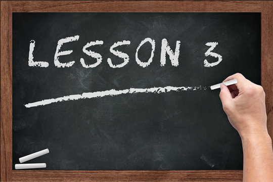 "Lesson 3" White chalk text write on chalkboard or school blackboard with male teacher hand hold chalk writing posture