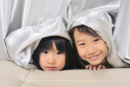 Two Asian Little Girls Peeking Out From A Curtain