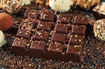 Bar of dark chocolate and candies on dark stone surface