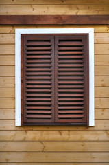 Detail of a wall of the wooden building with window and closed brown shutters.