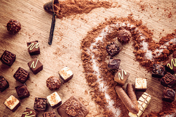 Delicious chocolate candies, truffles in a cocoa heart shape on the wooden background.