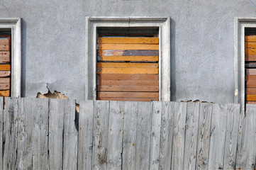 Facade of the destroyed building with boarded up window and wooden fence in the foreground.