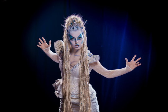 emotional actress woman in makeup and costume queen of elves or snow queen on blue-black background
