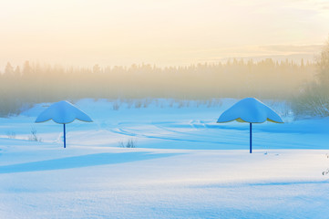 Beach umbrella on the bank of the frozen river. Foggy frosty morning.