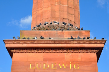 Ancient red column with an inscription "Ludewig" and sitting pigeons.