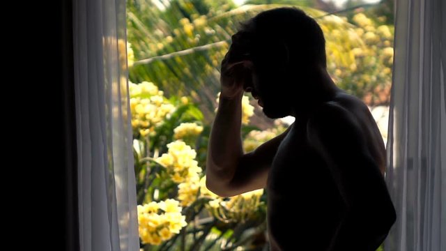Silhouette of sad, unhappy man standing by terrace window, super slow motion 240fps
