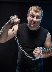 Actor Brutal man with a chain in his hands on a black background.