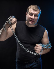 Actor Brutal man with a chain in his hands on a black background.