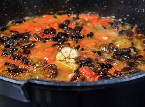 Pilaf on the cooking stage, zirvak with garlic, raisins, carrots, onions, lamb, barberry, saffron, zira and oil in a cauldron, boiling on the fire.
