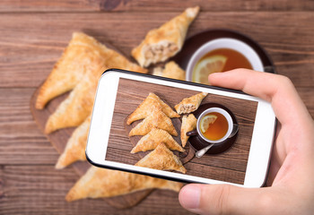 Hands taking photo homemade triangle meat pies with smartphone.