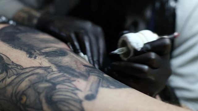 Tattoo master in black gloves, tattooing on the skin with black ink tattoo of his client in the salon.