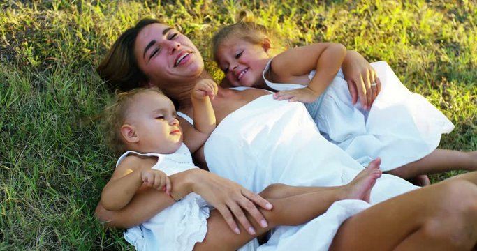 On a sunny day a mother playing with her baby daughter. Mom and daughter are surrounded by greenery and are very happy and srprigionano love and joy grinning and playing with each other