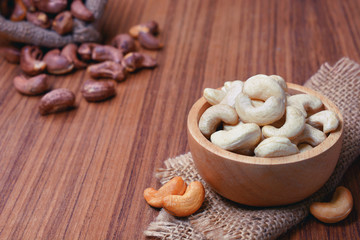 roasted cashew nuts with shell in gunny bag and on wooden background.