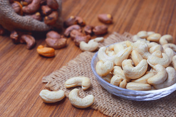 roasted cashew nuts with shell in gunny bag and on wooden background.
