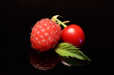 A raspberry and a cherry with a mint leaf
