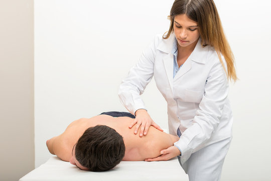 Female doctor physiotherapist practicing massage to her shoulder male patient in medical center.