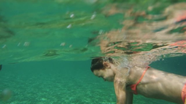 Girl diving underneath the surface in blue, turquoise  water. Shot from above and under the surface.