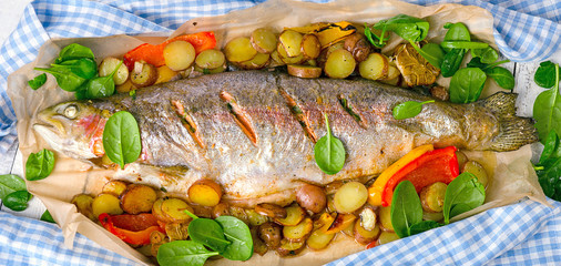 Whole salmon with vegetables on a paper on a table.