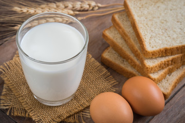 Milk glass with egg and bread on wooden table