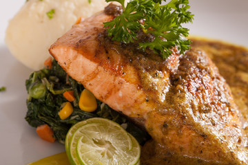 A nice dish of salmon steak served with mashed potato,lemon, saut&eacute; spinach and sauce on wood background