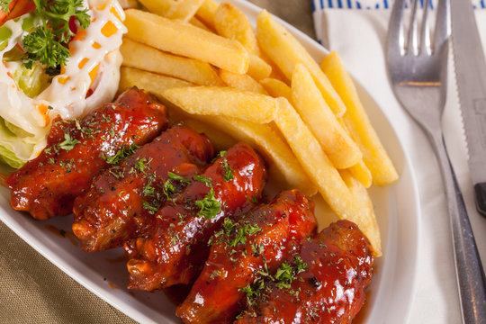 A dish of chicken wings with red barbecue sauce served in a nice decorated dish with french fries.