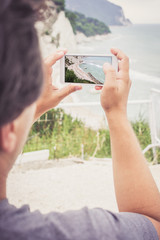 Young man taking photo of sea landscape on his cellphone