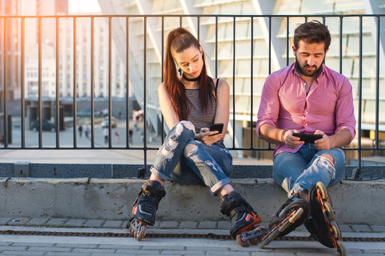 Man and woman holding phones. Inline skaters sitting. Give each other more attention.