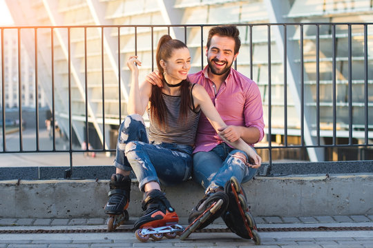 Smiling young couple on rollerblades. Woman and man sitting. New common hobby.