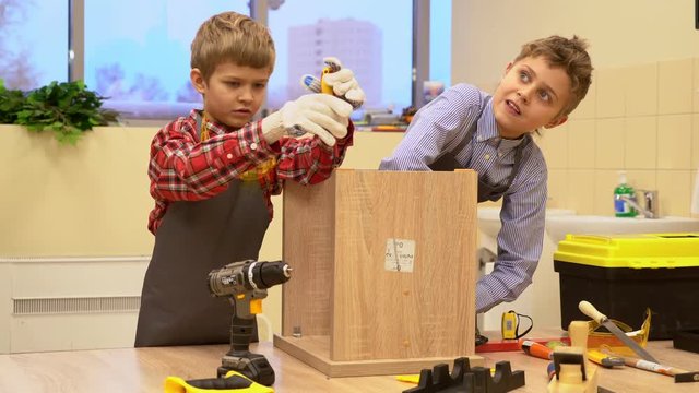 Two boys with screwdrivers and tools repairing wooden stool 