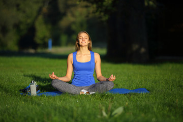 Smilling young woman sitting in lotus position on yoga mat in pa