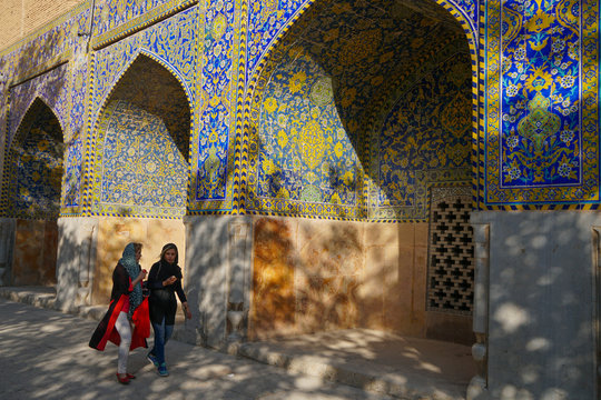 Two Iranian girls walking past courtyard walls, Imam Mosque, Isfahan, Iran